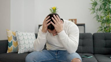 Young hispanic man stressed sitting on sofa at home