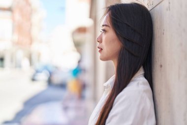 Genç Çinli kadın sokakta ciddi bir ifadeyle yan tarafa bakıyor.