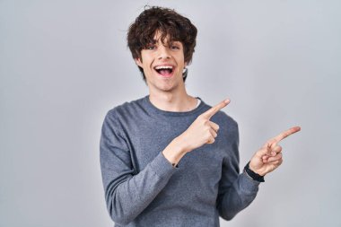 Arka planda duran genç adam gülümsüyor ve kameraya bakıyor iki eliyle ve parmaklarıyla kenarı işaret ediyor.. 