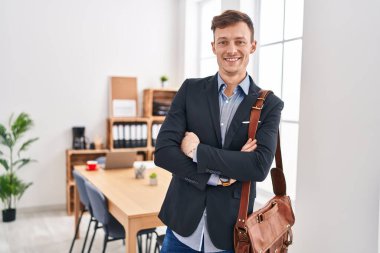 Genç iş adamı gülümsüyor. Kollarını kavuşturup ofiste kendine güveniyor.