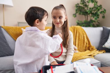 Doktor üniforması giyen sevimli bir kız ve erkek evlerinde steteskopla inceleme yapıyorlar.