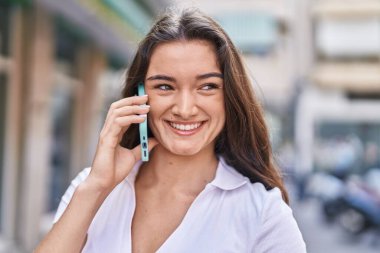 Young hispanic woman smiling confident talking on smartphone at street