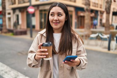 Genç İspanyol kadın akıllı telefon kullanıyor, sokakta kahve içiyor.