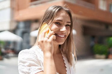 Beyaz bir kadın gülümsüyor ve caddede akıllı telefondan konuşuyor.