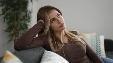 Kanepede oturan genç sarışın kadın. Şüpheli bir ifadeyle.