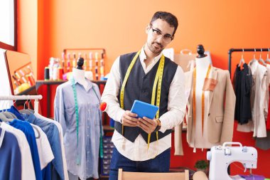 Young hispanic man tailor smiling confident using touchpad at atelier
