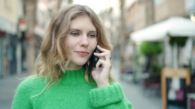 Kafe terasında rahat bir ifadeyle akıllı telefondan konuşan genç sarışın kadın.
