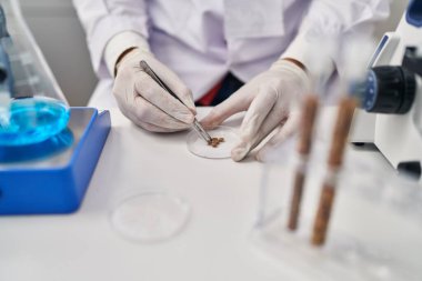 Genç İspanyol bilim adamı laboratuvarda cımbızla örnek tutuyor.