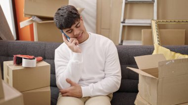 Genç İspanyol adam akıllı telefondan konuşuyor. Yeni evindeki kanepede oturuyor.