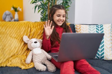 Adorable hispanic girl having video call sitting on sofa at home