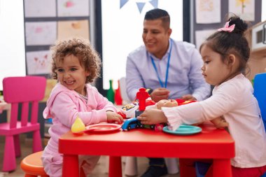 Anaokulundaki masada oturan İspanyol adam ve kızlar süpermarket oyunu oynuyorlar.