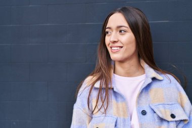 Genç, güzel İspanyol bir kadın, kendinden emin gülümsüyor ve izole edilmiş siyah bir arkaplanda yan tarafa bakıyor.