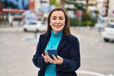 Sokakta akıllı telefon kullanan orta yaşlı bir iş kadını.