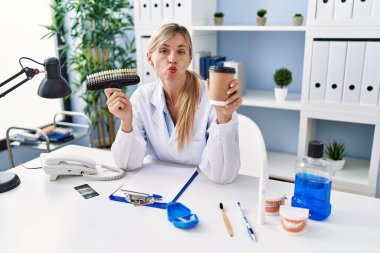 Güzel dişçi kadın takma diş ve diş fırçasıyla kameraya bakıyor. Öpücük atıyor, güzel ve seksi. aşk ifadesi. 