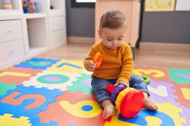 Anaokulunun zemininde oturan sevimli beyaz bebek halkalarla oynuyor.