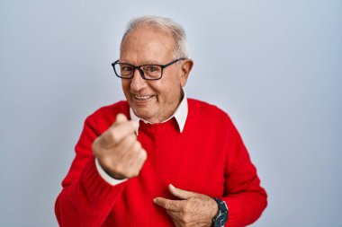 Gri saçlı yaşlı adam izole edilmiş arka planda dikiliyor. Buraya el hareketleriyle mutlu bir şekilde karşılamaya ve gülümsemeye davet ediyor. 