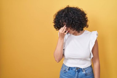 Ortadoğulu genç bir kadın sarı arka planda dikiliyor. Burnu ve gözleri ovuşturmaktan yorgun düşmüş. Yorgunluk ve baş ağrısı çekiyor. Stres ve hüsran kavramı. 