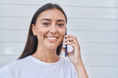 Genç, güzel, İspanyol bir kadın gülümsüyor. Akıllı telefondan kendine güvenen, izole beyaz arka planda konuşan.