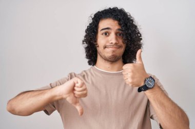 Beyaz arka planda duran kıvırcık saçlı İspanyol bir adam. Baş parmak kaldırıyor, anlaşamıyor ve anlaşamıyor. çılgın çatışma 