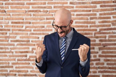 Sakallı, iş elbiseleri ve gözlüklü, mutlu ve heyecanlı bir adam kolları havada, gülümseyen ve başarı için bağıran, kazanan bir jest yapıyor. kutlama konsepti. 