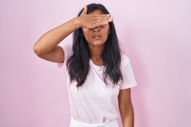 Pembe arka planda dikilen genç İspanyol kadın. Elle gözlerini kapatıyor. Ciddi ve üzgün görünüyor. Görme, saklama ve reddetme konsepti 