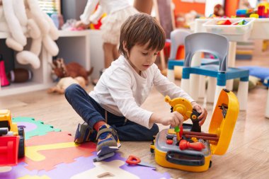 Sevimli beyaz çocuk anaokulunda yerde oturan aletlerle oynuyor.