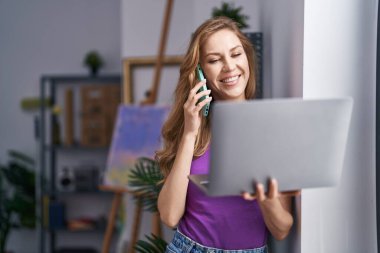 Sanat stüdyosunda dizüstü bilgisayarla konuşan genç sarışın bir sanatçı.