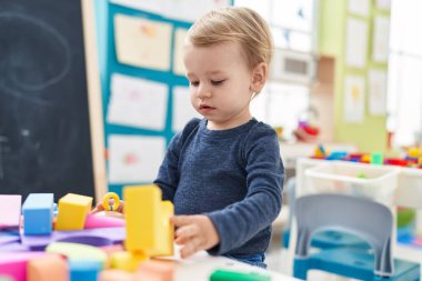Anaokulunda duran sevimli sarışın çocuk geometri bloklarıyla oynuyor.