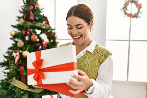 Young Beautiful Hispanic Woman Unpacking Gift Standing Christmas Tree Home — Stock Photo, Image