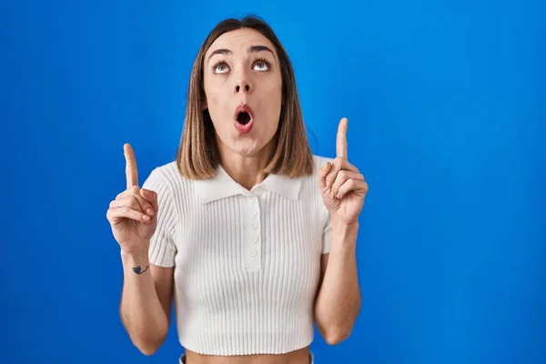 Hispanic Woman Standing Blue Background Amazed Surprised Looking Pointing Fingers — Stock Photo, Image