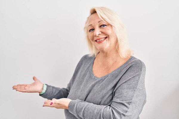 Middle age caucasian woman standing over white background inviting to enter smiling natural with open hand 
