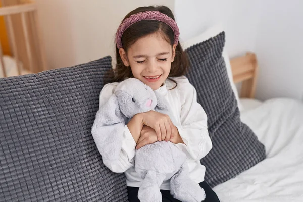 Sevimli Spanyol Kız Yatakta Oturmuş Oyuncak Bebeğe Sarılıyor — Stok fotoğraf