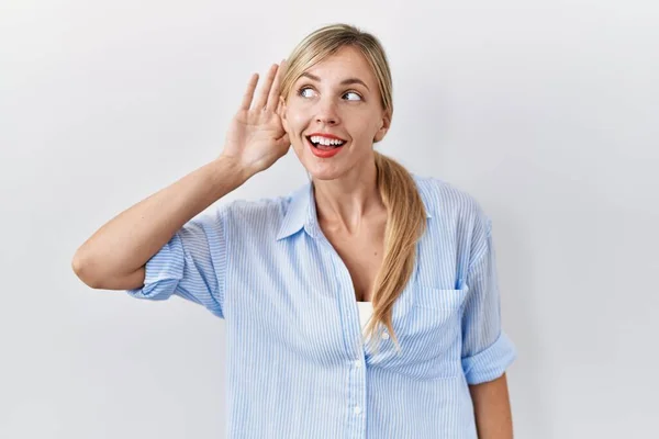 stock image Beautiful blonde woman standing over white background smiling with hand over ear listening an hearing to rumor or gossip. deafness concept. 