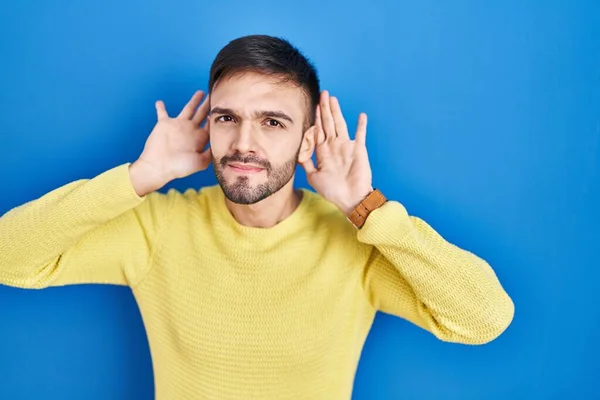 ヒスパニック系の男性の青い背景に耳のジェスチャーで両方の手を聞いて ゴシップを好奇心をしようと立っている 聴覚障害や聴覚障害 — ストック写真