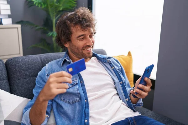 Joven Hombre Hispano Usando Teléfono Inteligente Tarjeta Crédito Sentado Sofá —  Fotos de Stock