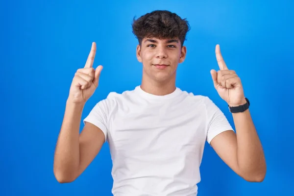 Adolescente Hispânico Sobre Fundo Azul Sorrindo Espantado Surpreso Apontando Para — Fotografia de Stock