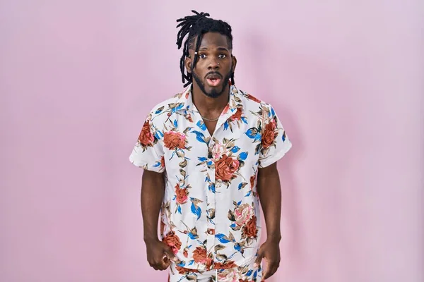 stock image African man with dreadlocks wearing summer shirt over pink background scared and amazed with open mouth for surprise, disbelief face 