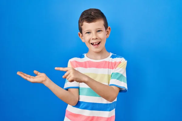 stock image Young caucasian kid standing over blue background amazed and smiling to the camera while presenting with hand and pointing with finger. 