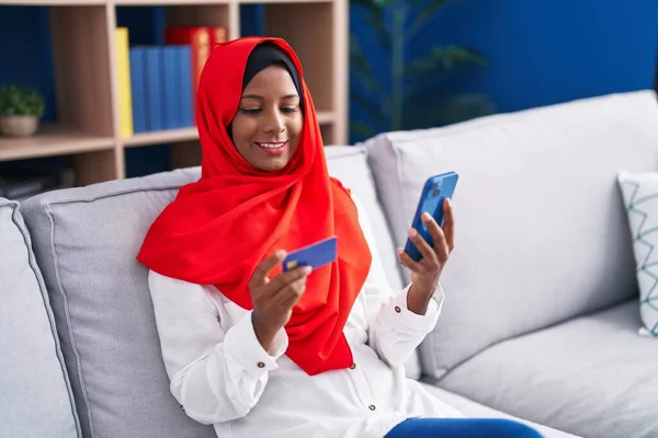 stock image Young beautiful woman using smartphone and credit card sitting on sofa at home