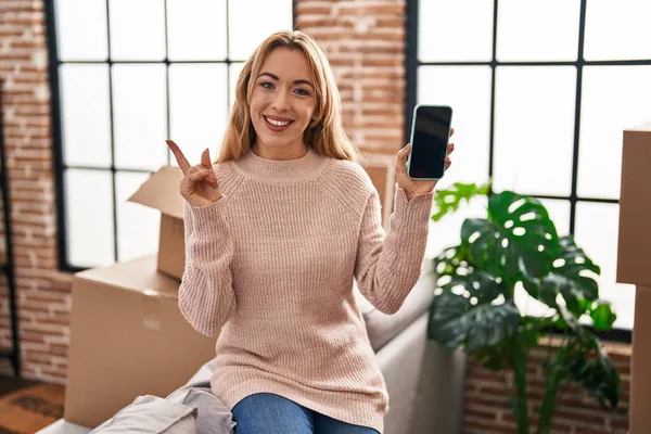 ヒスパニック系の女性に移動する新しい家を示すスマートフォンの画面笑顔幸せなポインティングとともに手と指で側面 — ストック写真
