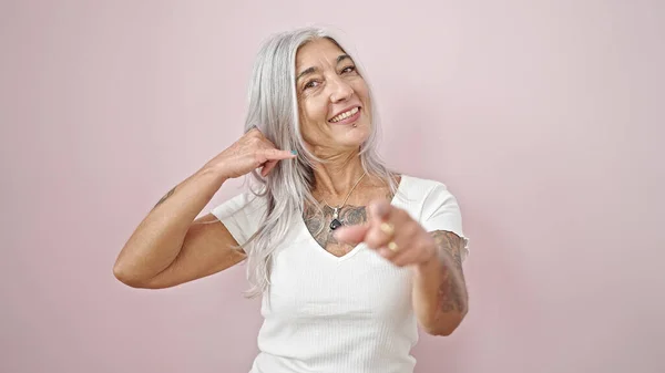 Middle age grey-haired woman smiling confident doing telephone gesture with hand over isolated pink background