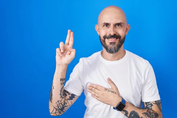 西班牙裔男子 身上有纹身 站在蓝色的背景上 微笑着 手托着胸膛和手指发誓 宣誓效忠 — 图库照片
