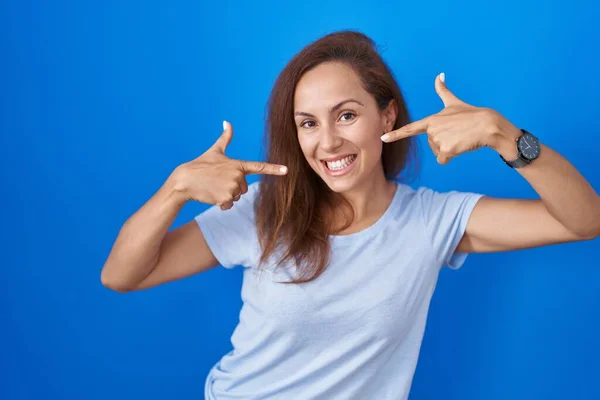 布鲁内特的女人站在蓝色的背景上 笑容满面 用手指 牙齿和嘴指指指点点 牙齿健康概念 — 图库照片