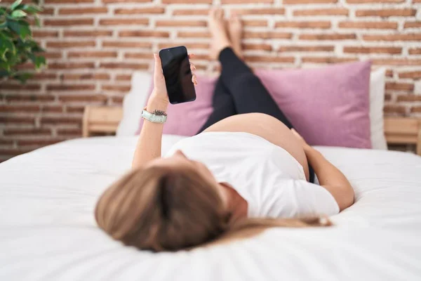 stock image Young pregnant woman using smartphone touching belly at bedroom