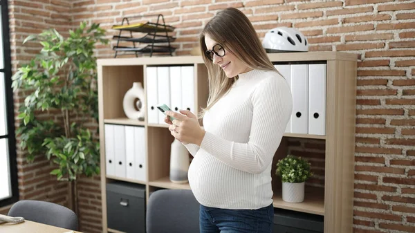 年轻的怀孕女工在办公室用智能手机摸肚子 — 图库照片