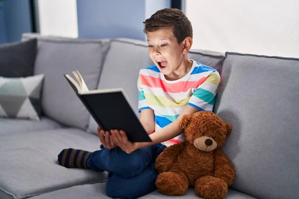 Niño Caucásico Joven Sentado Sofá Leyendo Libro Celebrando Loco Sorprendido —  Fotos de Stock