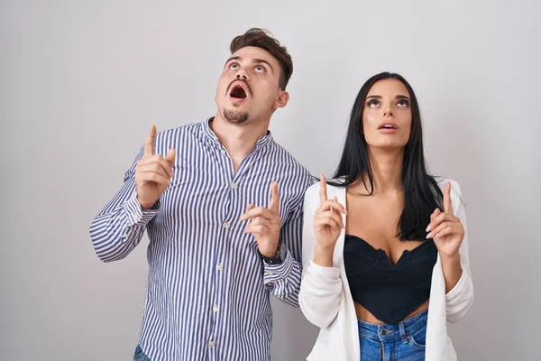 Young Hispanic Couple Standing White Background Amazed Surprised Looking Pointing — 스톡 사진