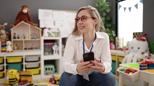 Młoda Blondynka Kobieta Przedszkolanka Uśmiecha Się Pewnie Pomocą Smartfona Przedszkolu — Zdjęcie stockowe