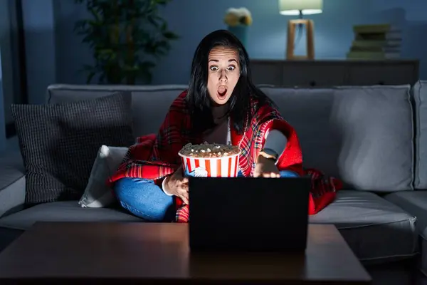 ヒスパニック系の女性ポップコーンを食べると ソファの上で指を前に驚いて映画を見て 口を開けて驚くような表現 フロントに何か — ストック写真