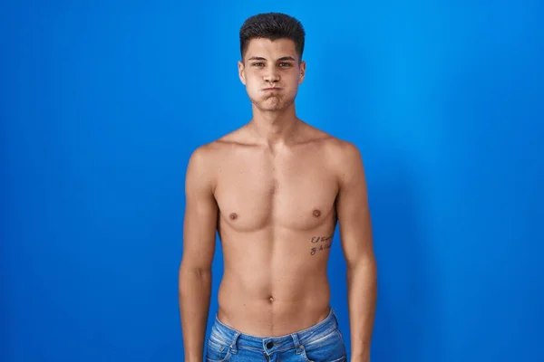 Joven Hombre Hispano Pie Sin Camisa Sobre Fondo Azul Soplando —  Fotos de Stock